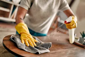 Gloved hand spraying and wiping down a wood surface, representative of Lumiora's deep cleaning service (stock photo)