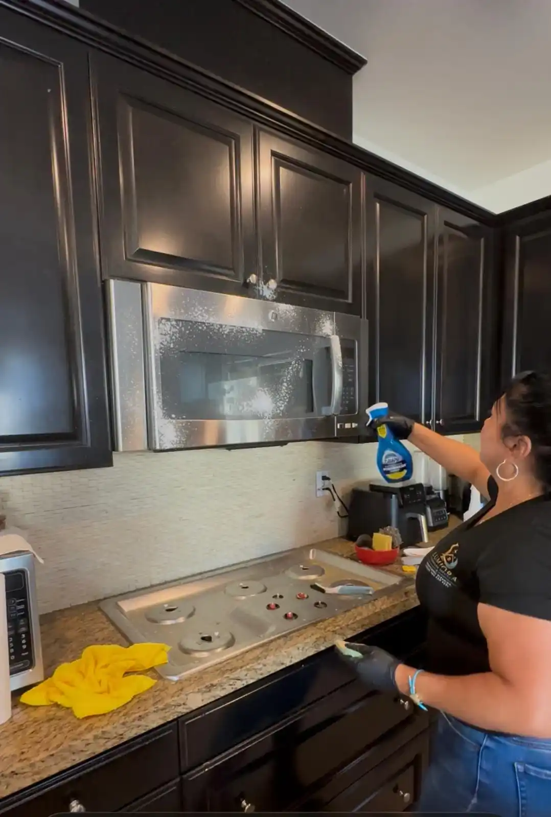 Lumiora team member cleaning a stainless steel microwave in a client kitchen