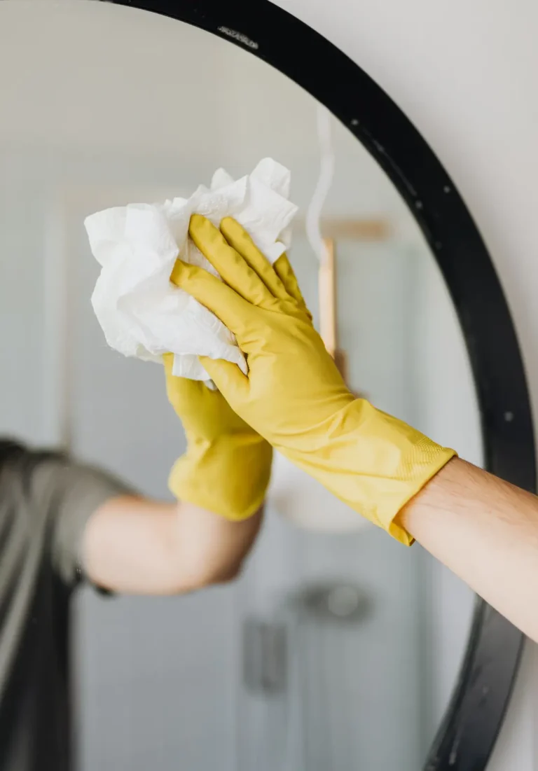 A gloved hand wiping a round mirror clean, representative of Lumiora's recurring cleaning service (stock photo)