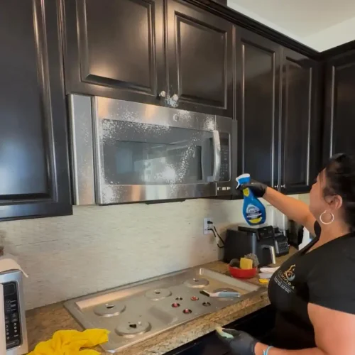 Lumiora team member cleaning a stainless steel microwave in a client kitchen